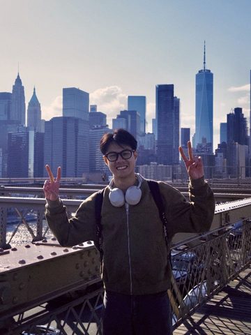 Clarence Boey on the Brooklyn Bridge, with the Lower Manhattan skyline behind him